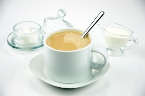 Coffee in a white cup served on a saucer with stirring spoon.